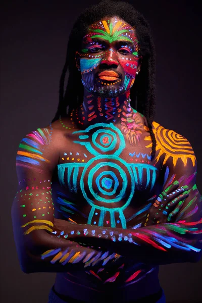 Hombre africano pintado en pintura fluorescente en la cara y el torso muscular —  Fotos de Stock