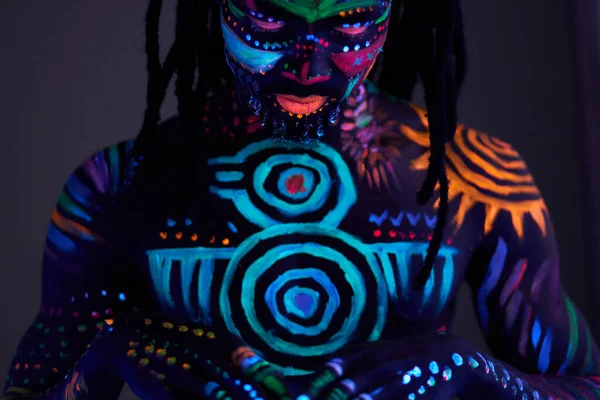 Afrikaanse man geschilderd in fluorescerende verf op gezicht en gespierde shirtloze romp — Stockfoto