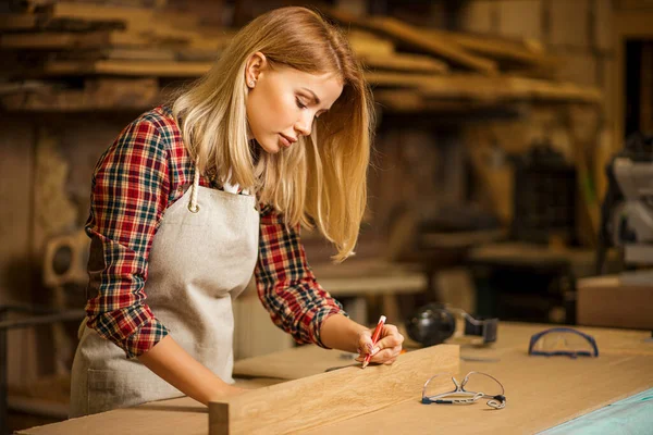 Hermosa mujer carpintera haciendo marcas en pieza de madera — Foto de Stock