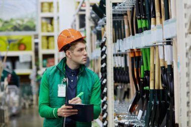 Depo çalışanı ürün verilerini karşılaştırır, bir belge okur ve notlar alır