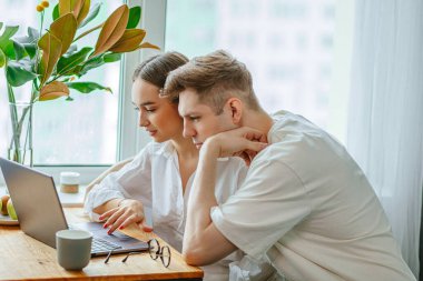 Genç beyaz çift evde dizüstü bilgisayarlarıyla oturuyor.