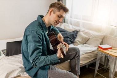Genç beyaz adam evde akustik gitar çalıyor.