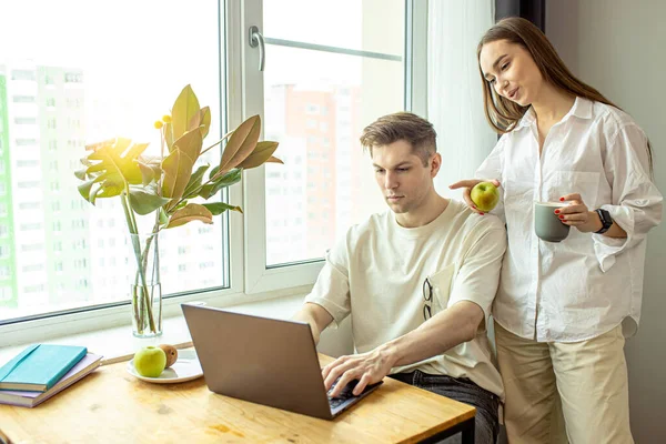 Mulher bonita apoiar seu marido enquanto trabalhar freelance em casa — Fotografia de Stock