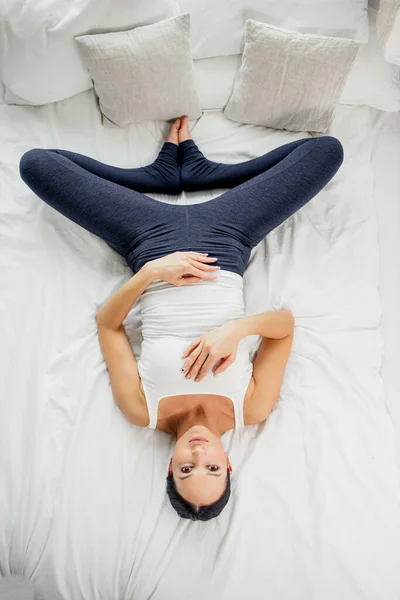 Flexibel kvinna i sportkläder tränar yoga på sängen — Stockfoto