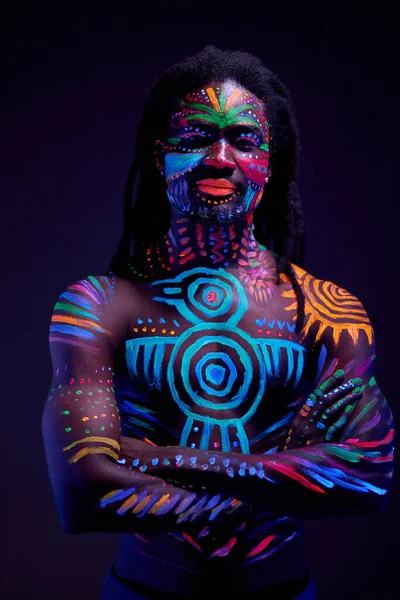 african man painted in fluorescent paint on face and muscular shirtless torso