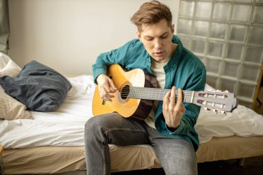 Genç erkek evde gitar çalıyor.