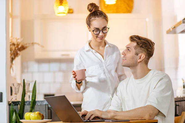 Mulher bonita apoiar seu marido enquanto trabalhar freelance em casa — Fotografia de Stock