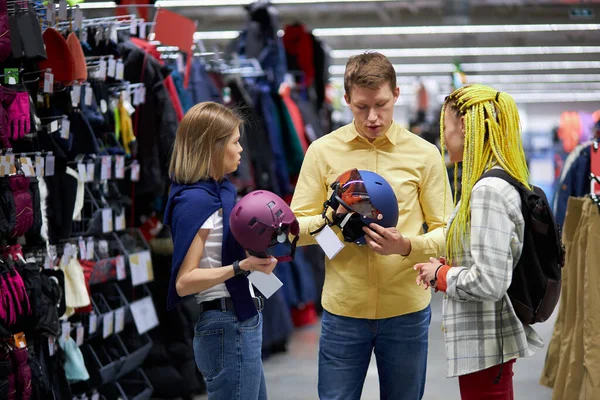 Drie Kaukasische vrienden gaan om helmen te kopen voor fietsen in sportkleding winkel — Stockfoto