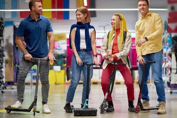 Homens e mulheres bonitos positivos usando scooters no corredor da loja — Fotografia de Stock