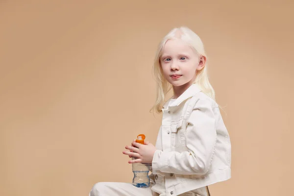 Gorgeous calm and shy albino child sitting with water bottle isolated — Stock Photo, Image