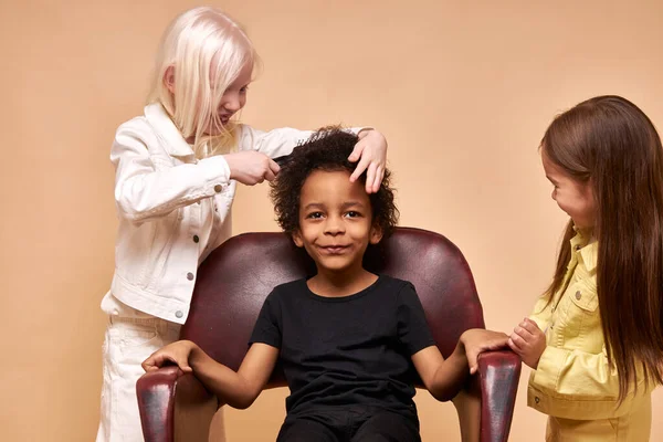 Menino preto sentar-se na cadeira como um rei, enquanto seus amigos pentear o cabelo — Fotografia de Stock