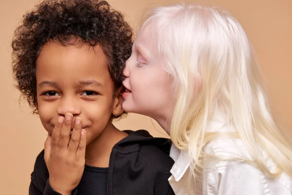 Albino menina conta um segredo no ouvido do menino africano multirracial — Fotografia de Stock