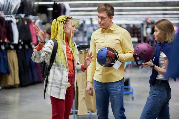 Três amigos caucasianos vão comprar capacetes para bicicletas na loja de roupas esportivas — Fotografia de Stock