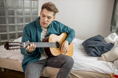 Genç erkek evde gitar çalıyor.