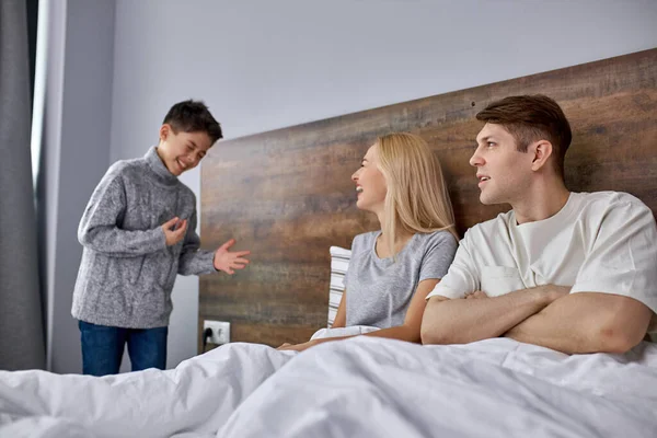 Sonrisa alegre positiva del niño mientras que habla con los padres en dormitorio —  Fotos de Stock