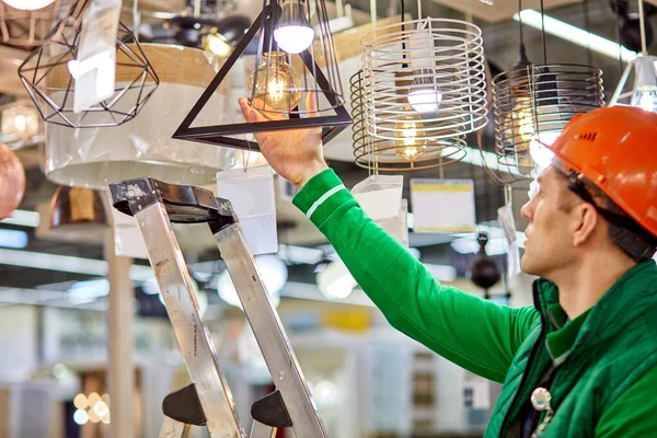창고에서 일하는 사람들은 새 사다리를 사용하여 램프의 전구를 점검 한다 — 스톡 사진