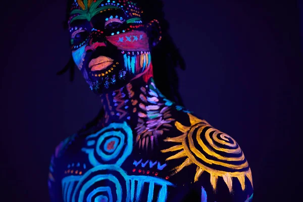 Retrato de hombre africano con patrón étnico, maquillaje de neón en luz ultravioleta —  Fotos de Stock