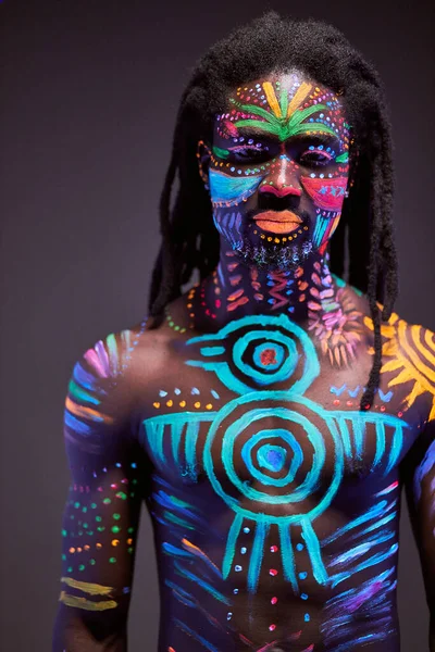 Hombre africano pintado en pintura fluorescente en la cara y el torso muscular — Foto de Stock