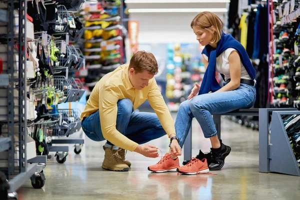 Полезный муж привязывает кроссовки к жене в магазине — стоковое фото