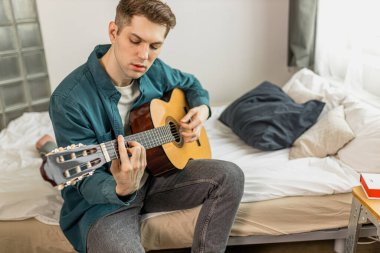 Yakışıklı adam evde gitar çalmaya çalışıyor.