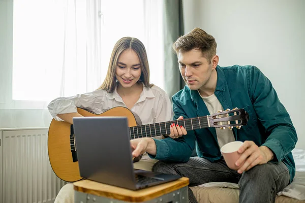 Atraente casal caucasiano assistir aulas de tocar guitarra usando laptop — Fotografia de Stock