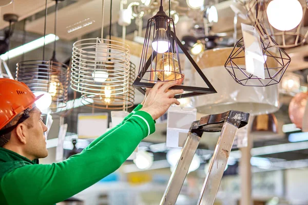 창고에서 일하는 사람들은 새 사다리를 사용하여 램프에서 전구를 깨고 있다 — 스톡 사진
