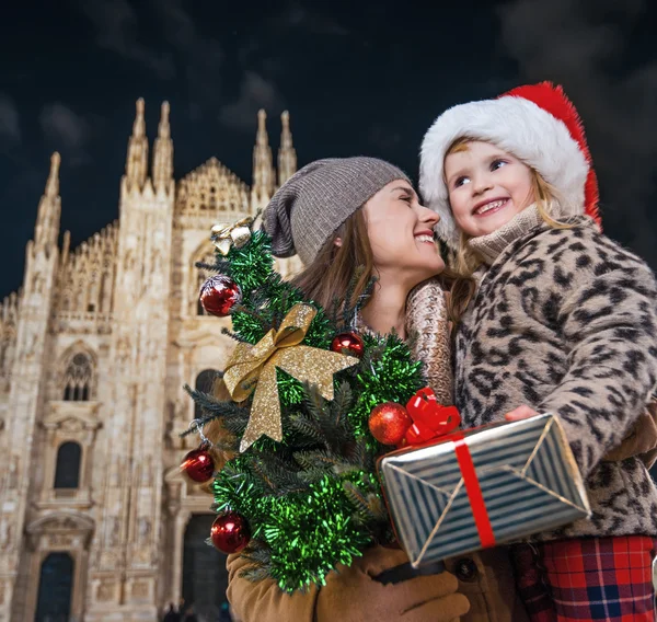 Smiling mother and daughter with Christmas tree and gift. Milan — Stockfoto