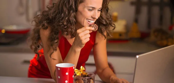 Glückliche junge Hausfrau mit Weihnachts-Snacks mit Laptop in Kitc — Stockfoto