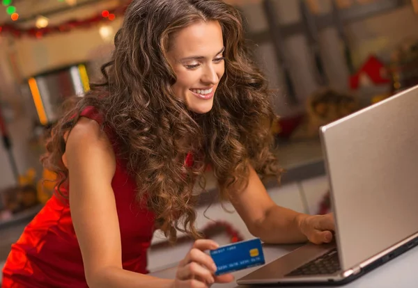 Femme avec carte de crédit tapant sur ordinateur portable dans la cuisine de Noël — Photo