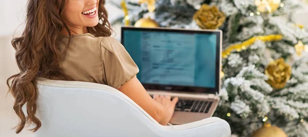 Усміхнена молода жінка використовує ноутбук біля ялинки — стокове фото