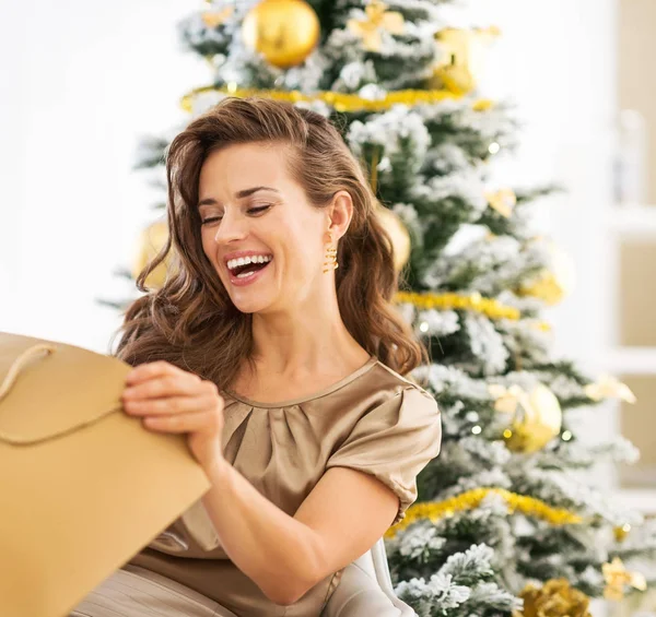 Усміхнена молода жінка дивиться в сумку біля різдвяної ялинки — стокове фото