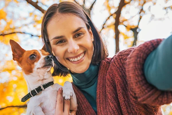 Uśmiechnięta młoda kobieta z psem na zewnątrz jesienią, Dokonywanie selfie — Zdjęcie stockowe