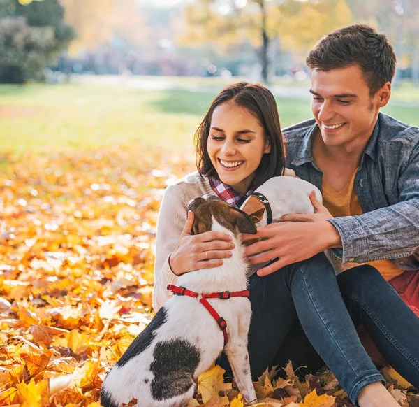 Retrato de feliz pareja joven sentada al aire libre en el parque de otoño a — Foto de Stock