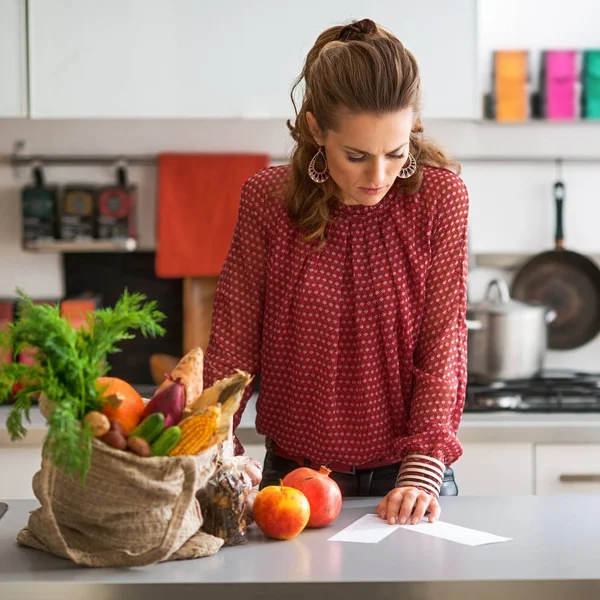 Жінка на кухні читає список покупок на лічильнику з покупками — стокове фото