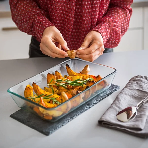 Primo piano sulla giovane casalinga aggiungendo aglio alla zucca al forno — Foto Stock