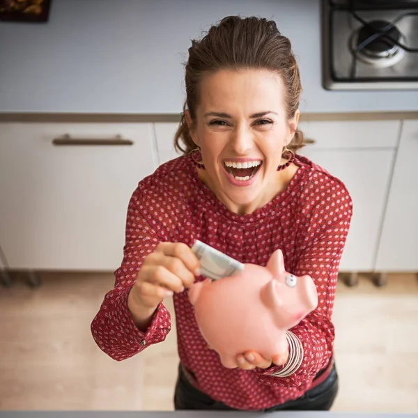 Happy young housewife putting money into piggy bank after shoppi — Stock Photo, Image