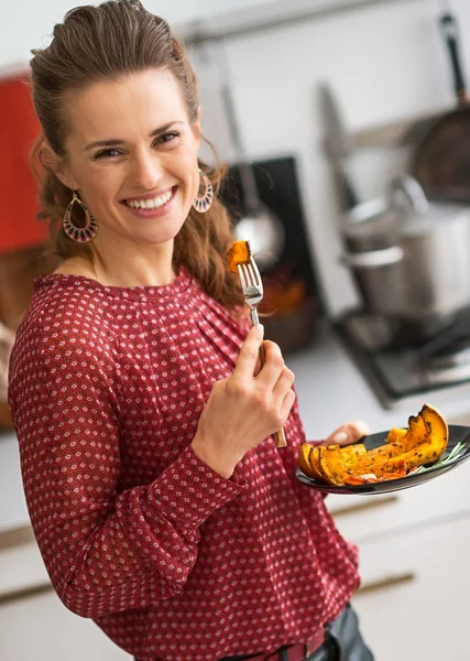 Junge Frau isst gebackenen Kürbis in Küche — Stockfoto