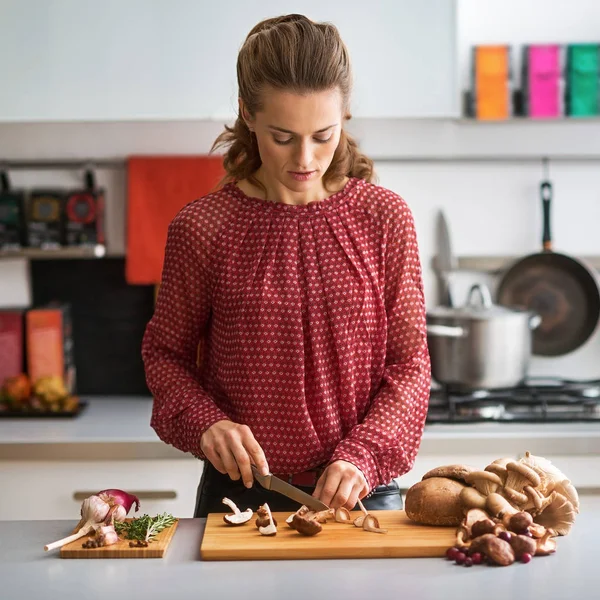 Jovem dona de casa cortando cogumelos na cozinha — Fotografia de Stock