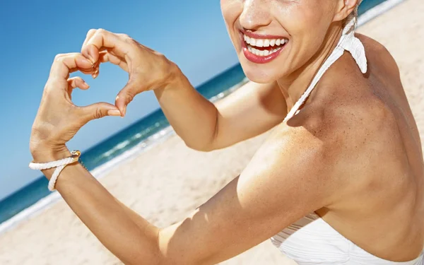 Mujer en traje de baño mostrando las manos en forma de corazón en la playa de arena —  Fotos de Stock