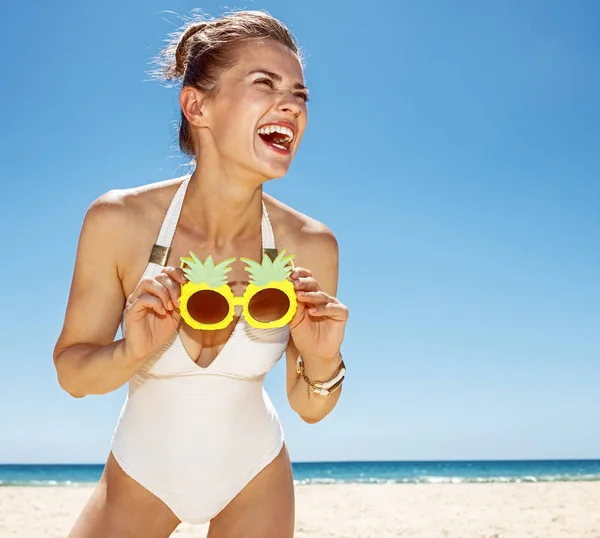 Mosolygó nő a gazdaság szemüveg funky ananász homokos strand — Stock Fotó