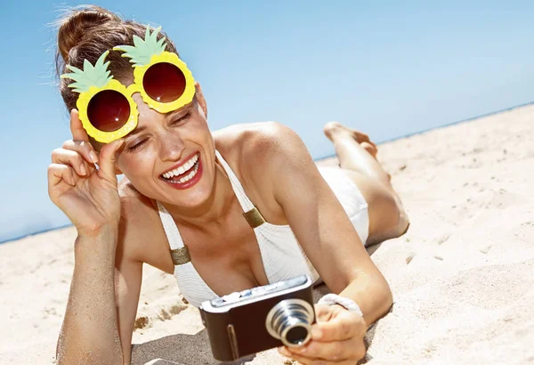 Woman in pineapple glasses checking photo at sandy beach — Stock Photo, Image