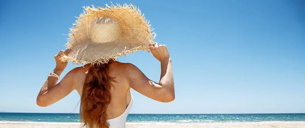 Seen from behind woman in white swimsuit and straw hat at beach — Stock Photo, Image