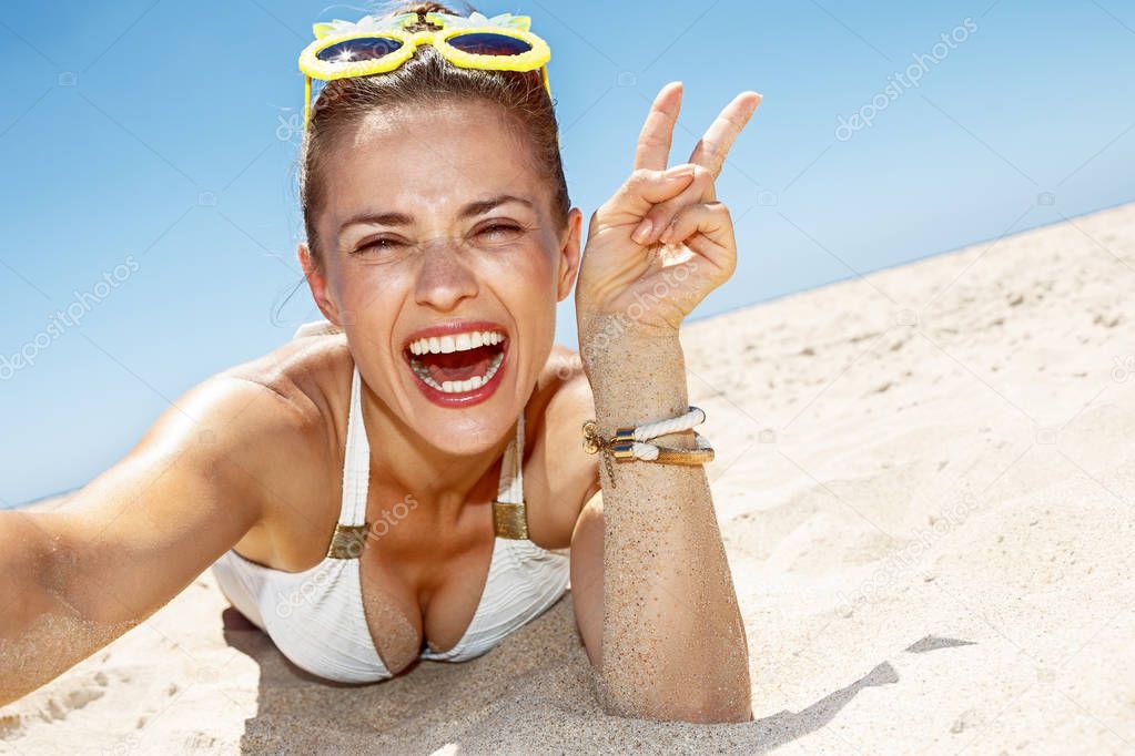 Woman taking selfies and showing victory gesture at sandy beach