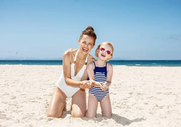 Lycklig mor och barn på stranden visar händerna fulla av sand — Stockfoto