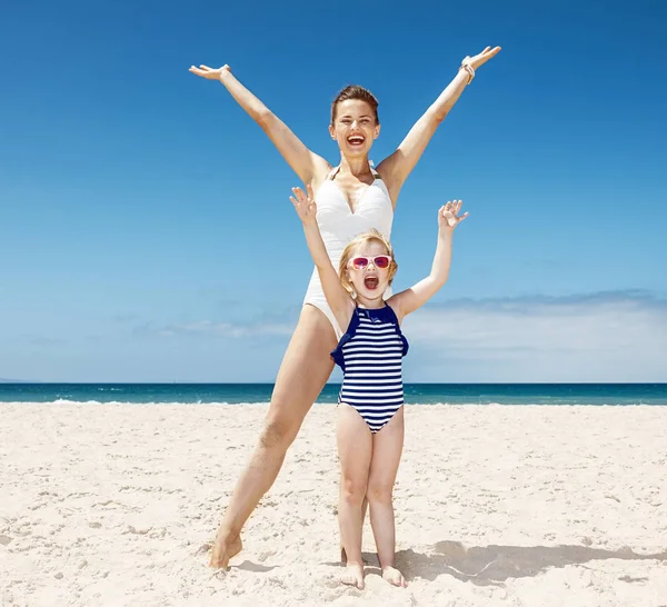 Boldog anya és a gyermek az örvendezés homokos strand fürdőruhák — Stock Fotó