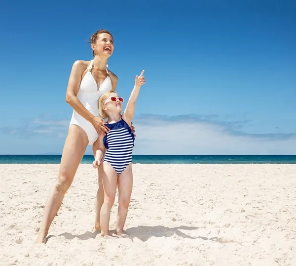 Boldog anya és a gyermek mutatva-hoz valahol, homokos strand — Stock Fotó