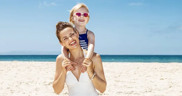 Feliz madre y niña en trajes de baño en la playa de arena en un día soleado —  Fotos de Stock