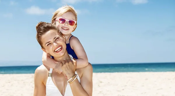 Bonne mère et son enfant en maillot de bain à la plage de sable le jour ensoleillé — Photo