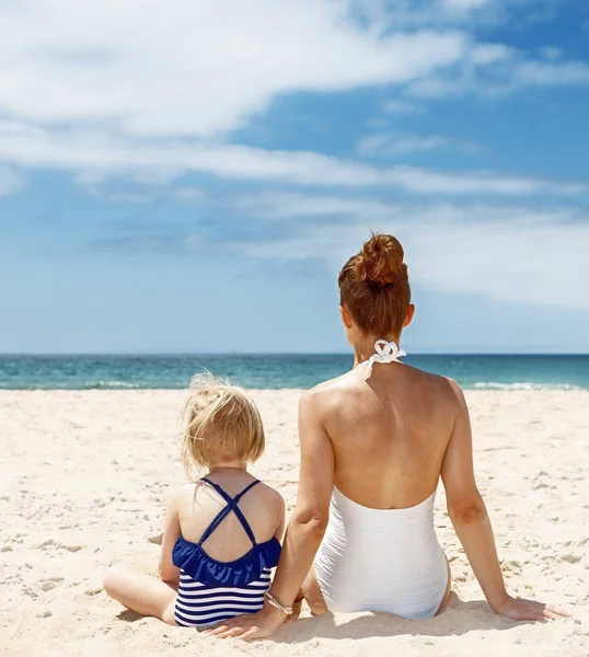 Gezien achter het moeder en kind in zwemkleding zittend op het strand — Stockfoto