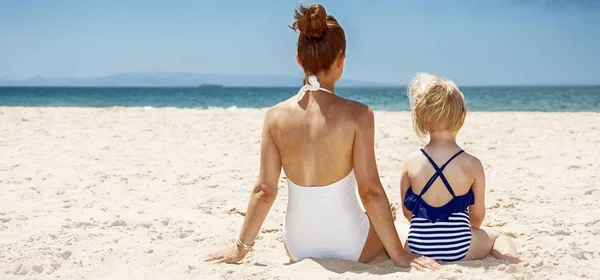 Vu de derrière mère et enfant en maillots de bain assis à la plage — Photo